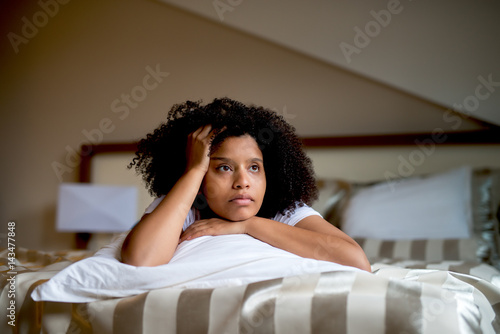 Cuadro en lienzo Sad curly black girl lying on bed hugging white pillow.