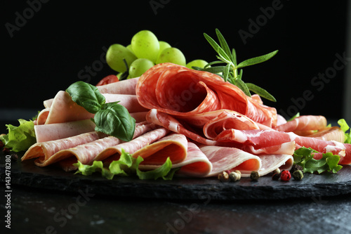 Food tray with delicious salami, pieces of sliced ham, sausage, tomatoes, salad and vegetable - Meat platter with selection