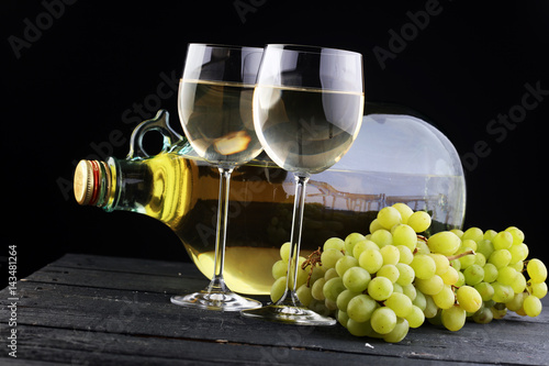 Bottle and glass of white wine, grape on wooden table