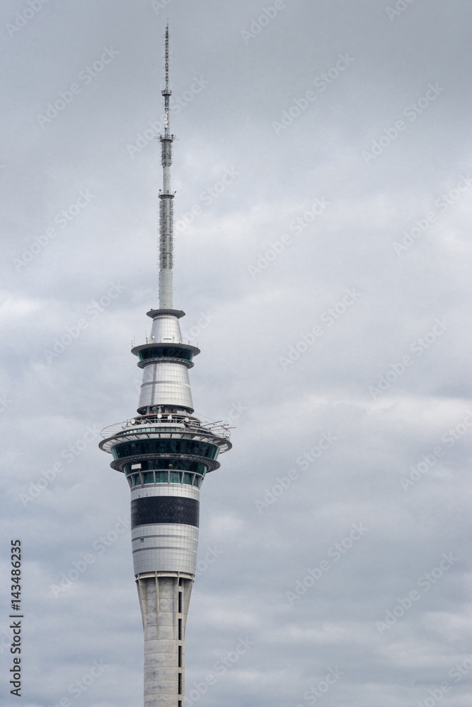 Auckland, New Zealand - March 1, 2017: The top half of the sky tower against gray cloudy sky shows the shaft, the restaurant, the bungee platform and the antenna and communication installation.