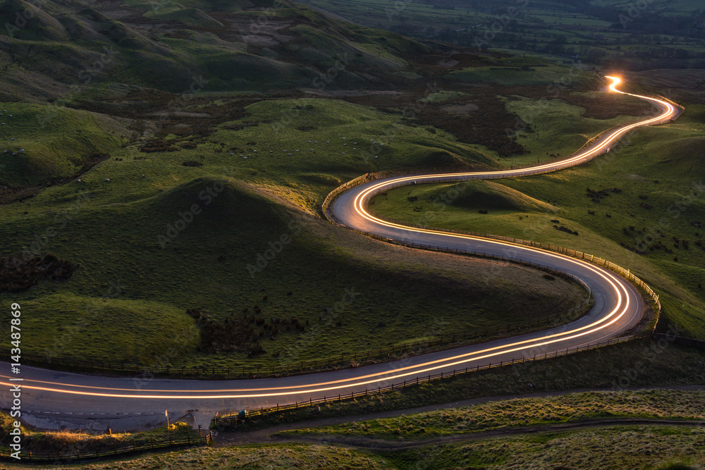 Winding curvy rural road with light trail from headlights leading through British countryside. - obrazy, fototapety, plakaty 