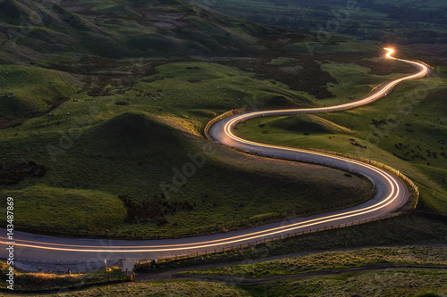 Winding curvy rural road with light trail from headlights leading through British countryside.