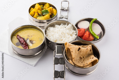 indian typical stainless steel lunch box or tiffin with north indian or maharashtrian food menu like chapati//roti, dal tadka, white rice and aloo / potato sabji / gobi or cauliflower sabji with salad