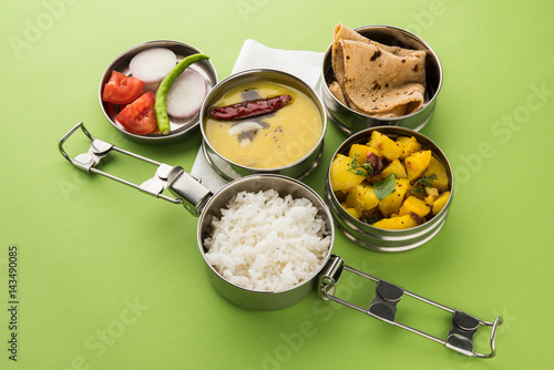 indian typical stainless steel lunch box or tiffin with north indian or maharashtrian food menu like chapati//roti, dal tadka, white rice and aloo / potato sabji / gobi or cauliflower sabji with salad photo