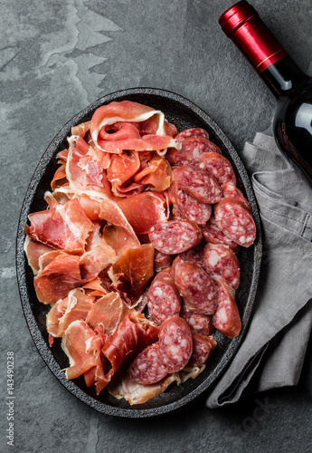 Plate of spanish jamon serrano and salami and bottle of red wine on slate background. Top view
