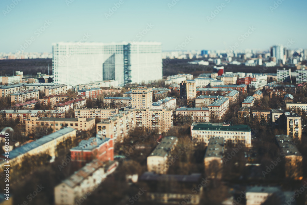 Close-up tilt shift shooting from high point of residential district of metropolitan city on sunny spring day with multiple small houses and one huge in blurred distance, clear teal horizon and sky