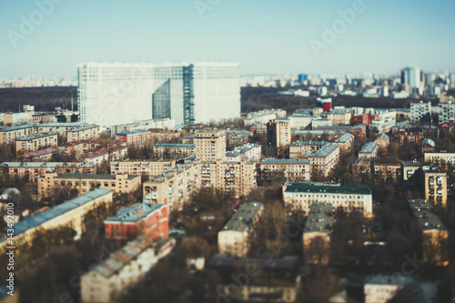 Close-up tilt shift shooting from high point of residential district of metropolitan city on sunny spring day with multiple small houses and one huge in blurred distance, clear teal horizon and sky