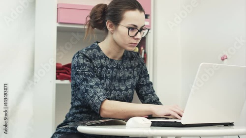 Beautiful young female showroom owner working using laptop computer and fashion magazine photo