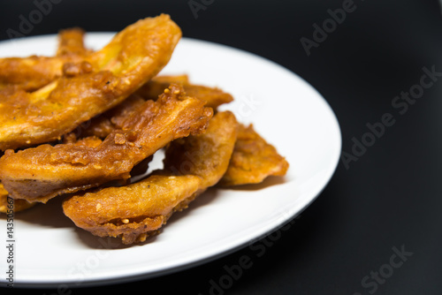 Delicious traditional golden fried banana fritters on white plate with black background isolated