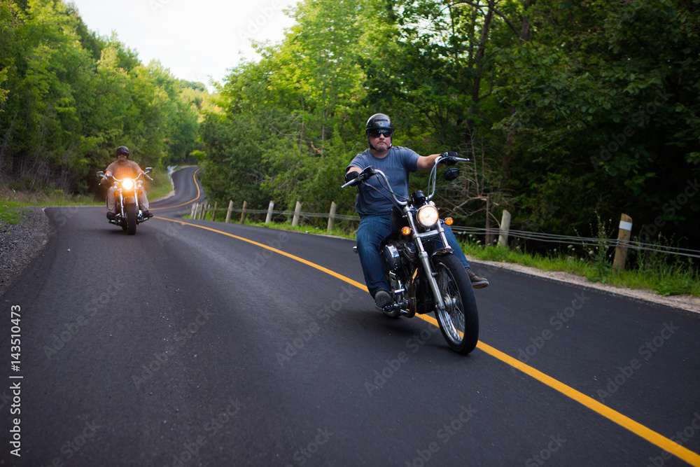 Two friends riding motorcycles on country road
