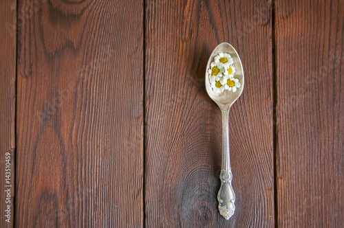 Obraz na plátně Small chamomile flowers in a melchior tea spoon on a wooden background