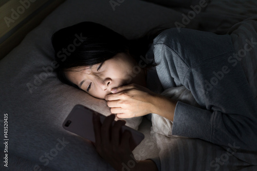 Woman feeling tired and using mobile phone on bed