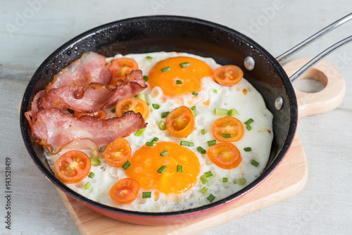 Pan of fried eggs, bacon and tomato.