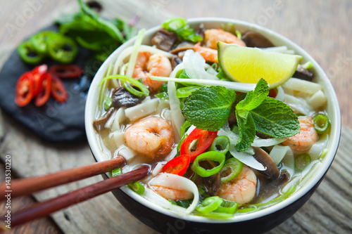 Vietnamese Pho Tom  Rice Noodles Soup with King Prawns. Asian cuisine cooking spices: ginger, lime, chili, garlic, spring onions,lemon grass,  chives, shallots, mint and Shiitake mushrooms. 