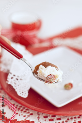 Baba with a cream and strawberries on spoon red and white colors