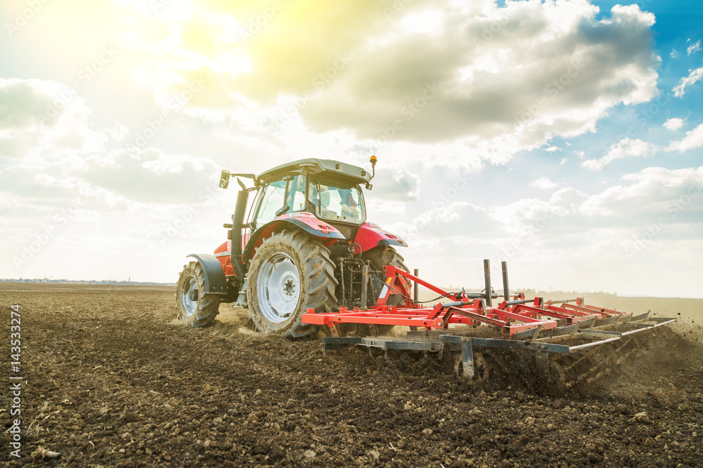 Obraz premium Farmer in tractor preparing land with seedbed cultivator as part of pre seeding activities in early spring season of agricultural works at farmlands.
