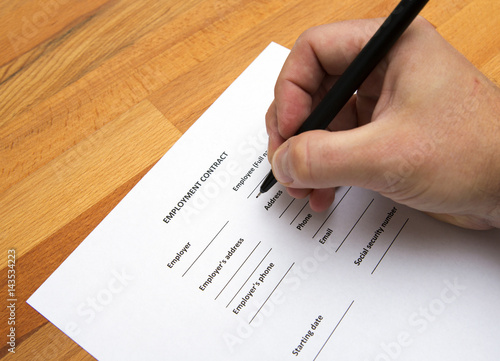 A person is writing an employment agreement with a pen on a wooden table. Business concept image.