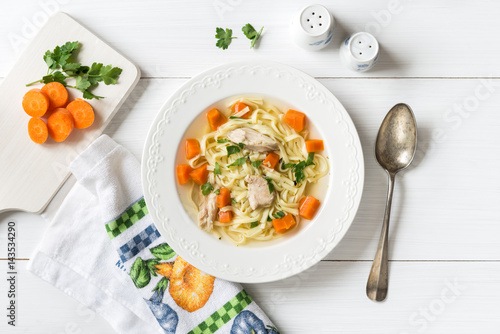 Top view of chicken soup with pasta, carrot and parsley on white table