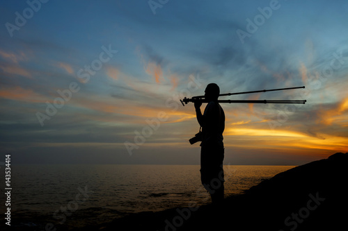 Silhouette of a photographer or traveler with tripod standing on stone ,sunset time.