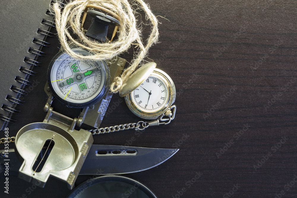 Pocket knife with compass,paper,pencil,notebook,pocket watch,rope,magnifying glass on black wood background Pocket knife with compass,paper,pencil,notebook,pocket watch,rope,magnifying glass on black wood background