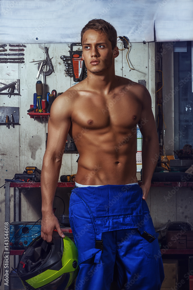 Sexy auto mechanic man stands on a background of tools holding a