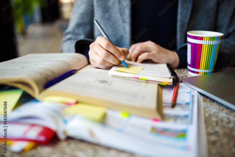 Shot of young male student sitting at table and writing on notebook. Young male student studying in cafe Shot of young male student sitting at table and writing on notebook. Young male student studying in cafe