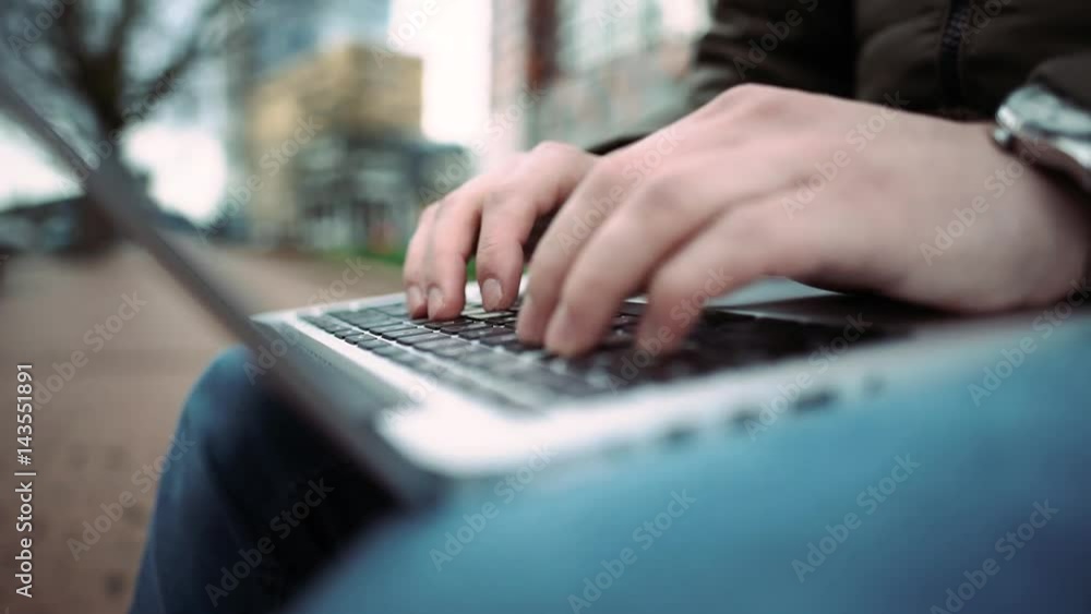 Young man using his laptop on a street bench man typing on his laptop. View from top. 4k. Detail hand Young man using his laptop on a street bench man typing on his laptop. View from top. 4k. Detail hand