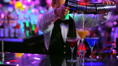 club: a bartender pours colorful cocktails 3 glasses at once.