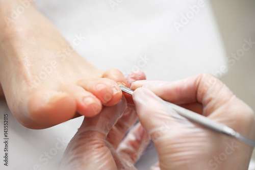 Pedicure. Kosmetyczka wykonuje zabieg pedicure, czyści i obcina paznokcie u stóp photo