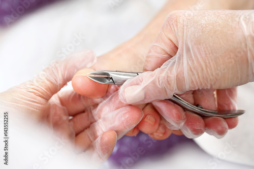 Etapy wykonywania pedicure. Kosmetyczka wycina cążkami skórki przy paznokciach i wykonuje profesjonalny pedicure.
