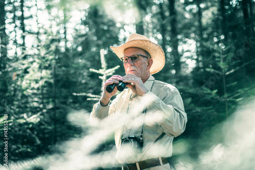 Retired man with binocular in forest.