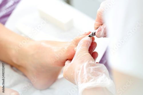 Obcinanie paznokci u stóp, kobieta na zabiegu pedicure. Kosmetyczka wycina cążkami skórki przy paznokciach i wykonuje profesjonalny pedicure.