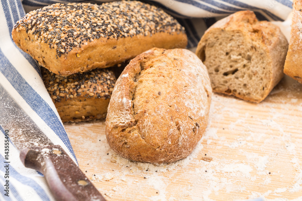 Fototapeta premium Whole wheat bread buns and slices, on wooden surface with flour.