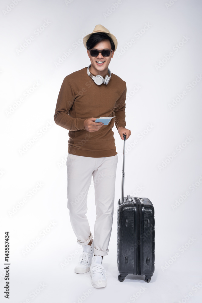 Full length of young tourist asian man holding passport with suitcase over grey background Full length of young tourist asian man holding passport with suitcase over grey background