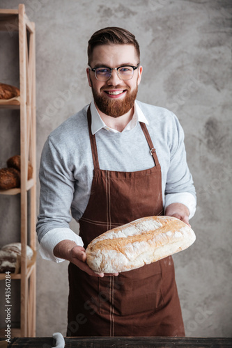 Cheerful young man baker standing at bakery holding bread