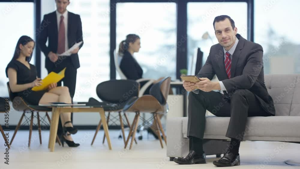 Portrait smiling businessman in office with colleagues working in background Portrait smiling businessman in office with colleagues working in background