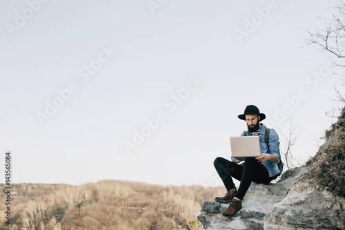 handsome bearded man freelancer working on a laptop outdoors in mountains. Freelance concept