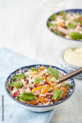 a bowl of rice salad with ham stripes, broken almonds, dried cranberries and orange