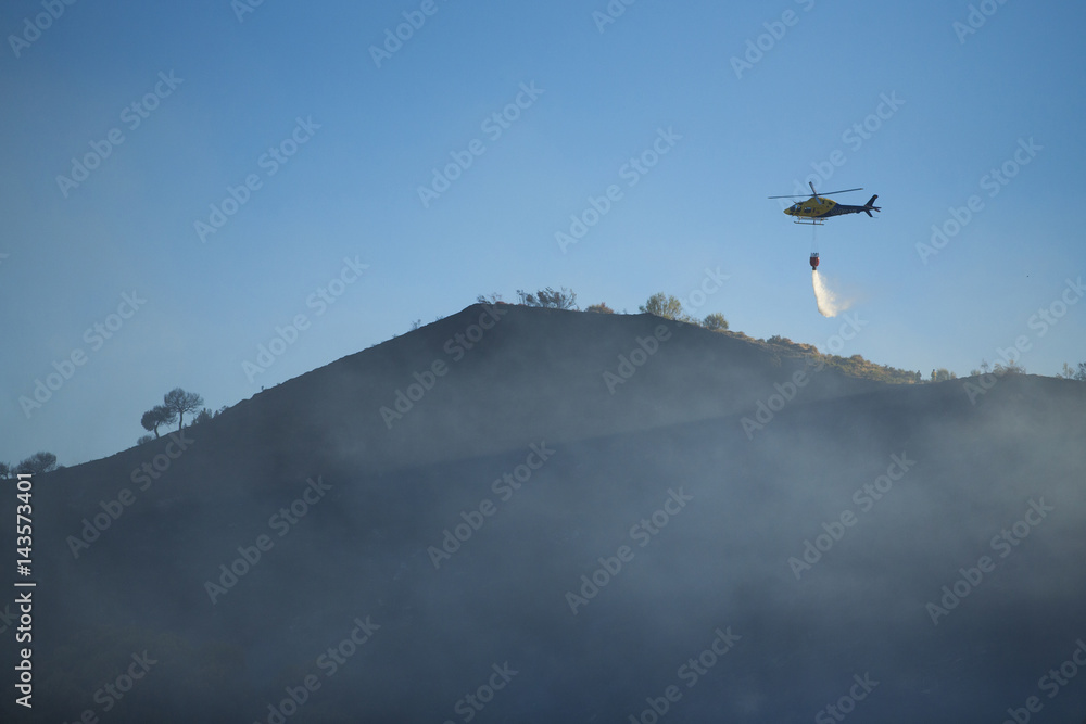 Fototapeta premium GRANADA, AUGUST 28: Fire fighting Helicopter, with bambi basket, during a fire fighting in the bush. August 28, 2014, Granada, Spain.