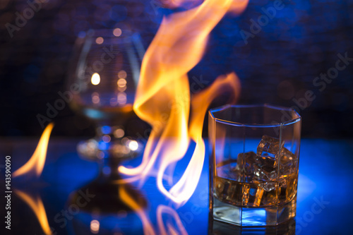 Glass o whisky with ice and wineglass of coghac and fire flames on bokeh background