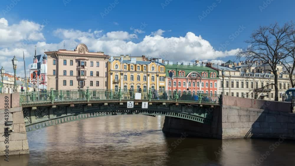 View to the First Engineer Bridge on the Moyka River and red and yellow Olsufiev's houses in the background. Sunny day, blue sky with cumulus clouds. Saint-Petersburg, Russia. View to the First Engineer Bridge on the Moyka River and red and yellow Olsufiev's houses in the background. Sunny day, blue sky with cumulus clouds. Saint-Petersburg, Russia.