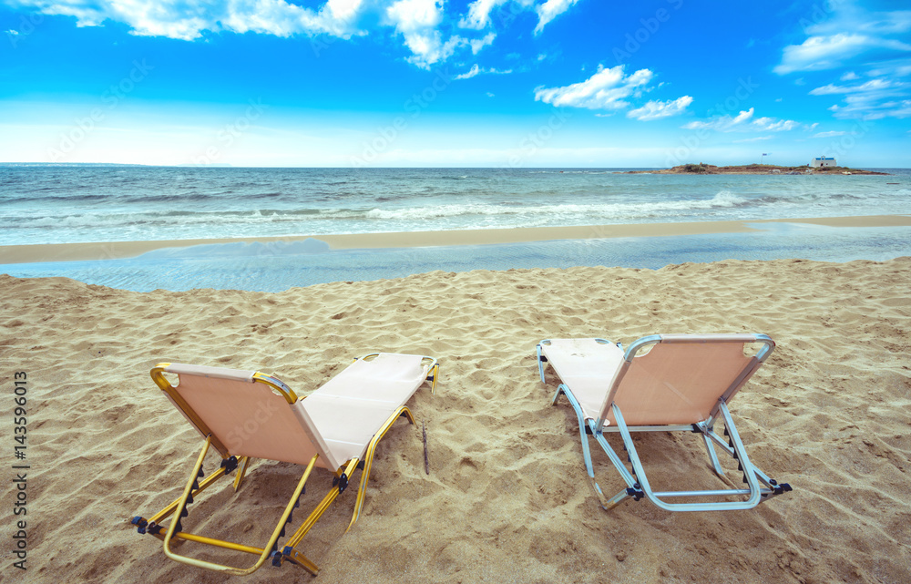 Typical summer image of an amazing pictorial view of a sandy beach with sun beds and an old white church in a small island at the background, Malia, Crete, Greece. Typical summer image of an amazing pictorial view of a sandy beach with sun beds and an old white church in a small island at the background, Malia, Crete, Greece.