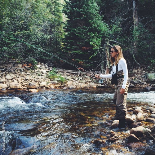 Young woman fly fishing along a Colorado stream