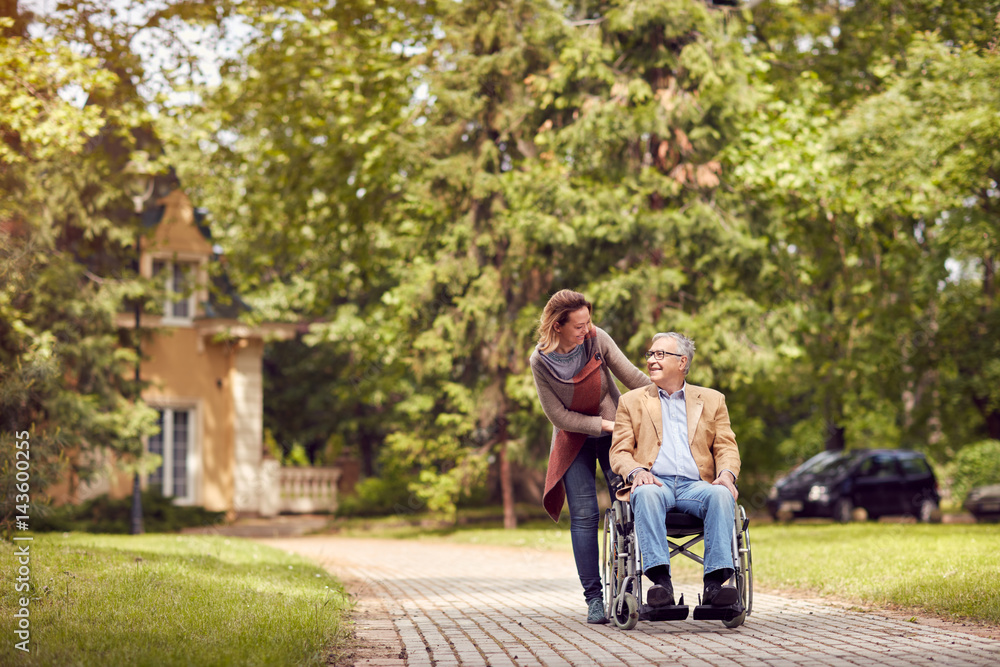© luckybusiness - daughter and senior man in wheelchair on walking green nature.