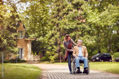 daughter and senior man in wheelchair on walking green nature.