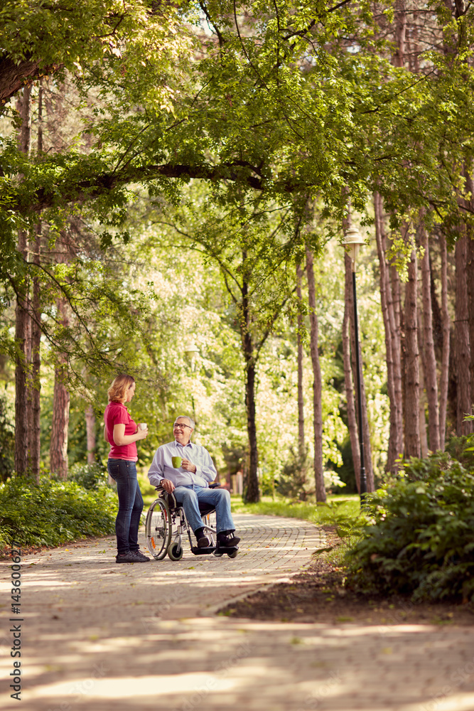 woman with her disabled happy father in wheelchair enjoying time together in the park. woman with her disabled happy father in wheelchair enjoying time together in the park.