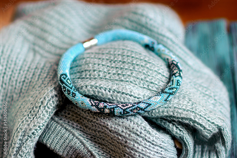 Fototapeta premium beautiful blue bracelet lies on a knitted scarf, female costume jewelry, gifts to girls