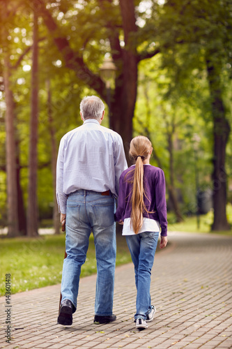 Girl and her grandfather holding hands on walk.