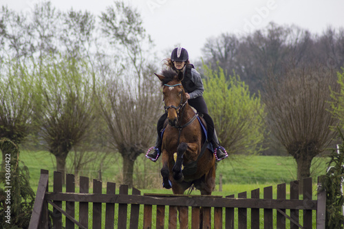 cross county horse jumping over bars by teenager girl
