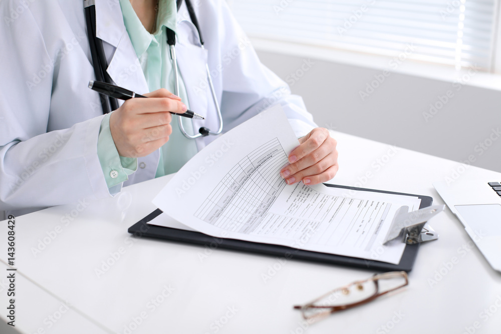Close-up of a female doctor filling out application form , sitting at the table in the hospital Close-up of a female doctor filling out application form , sitting at the table in the hospital